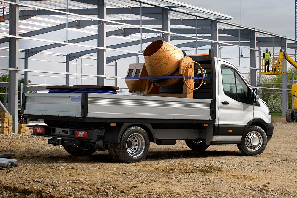 Ford Transit châssis-cabine transportant une bétonnière sur son plateau, stationné sur un chantier. 