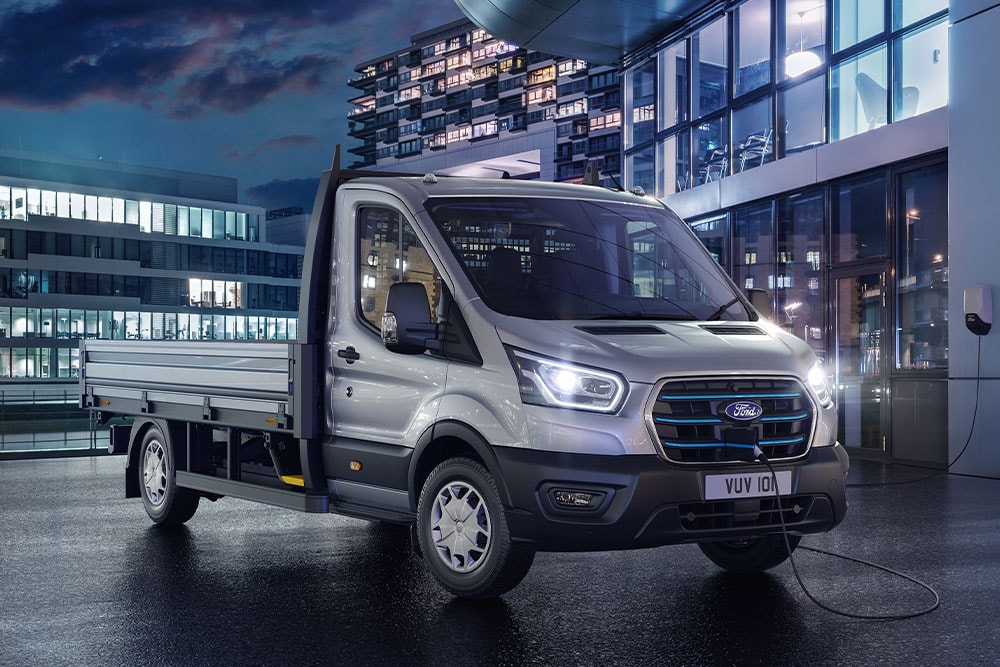 Ford E-Transit châssis-cabine argenté stationné devant un bâtiment moderne, de nuit.
