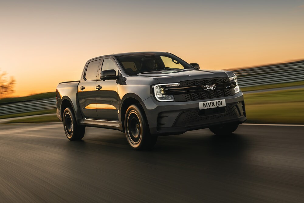 Un Ford Ranger Platinum gris foncé roule sur une piste au coucher de soleil.