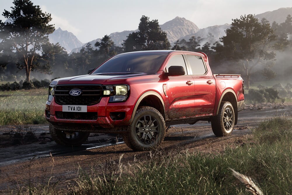 Un Ford Ranger Raptor rouge roulant sur un chemin de terre à travers un paysage pittoresque.