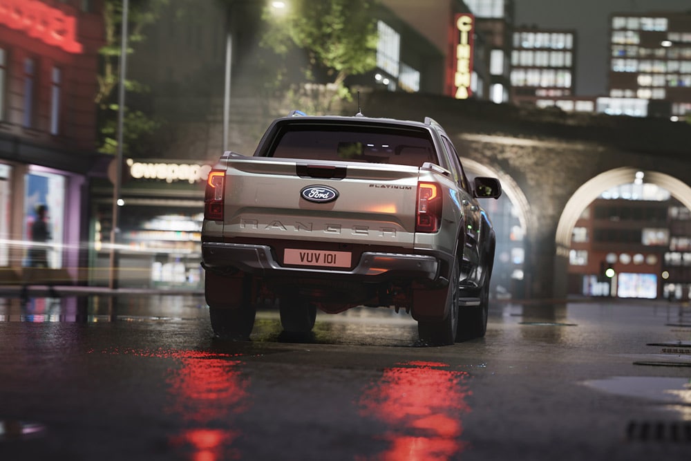 Vue arrière d’un Ford Ranger argenté circulant de nuit dans un paysage urbain illuminé par des néons.