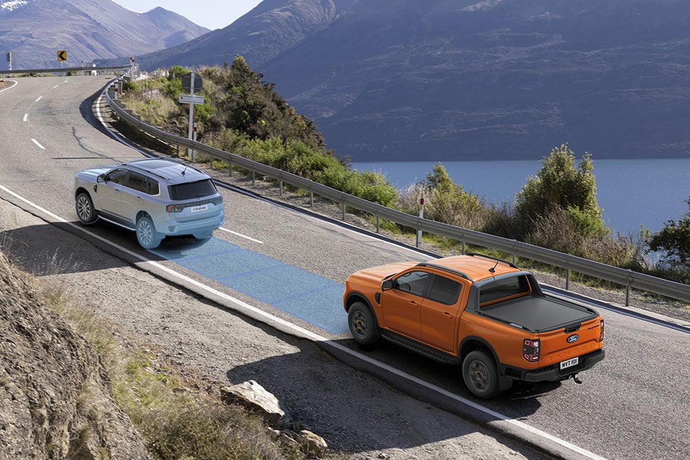 Un Ford Ranger orange utilise son système avancé d’aide à la conduite sur une autoroute côtière. 