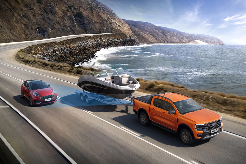 Un Ford Ranger orange tracte un bateau sur une autoroute côtière, démontrant sa capacité de remorquage.