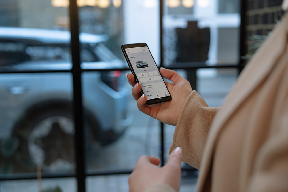Une personne tenant un smartphone affichant l’application FordPass avec des informations sur la gestion de flotte.