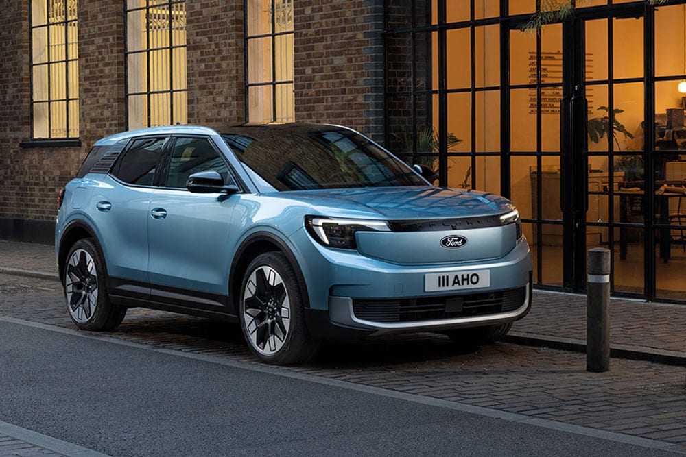 Vue latérale d’un Ford Explorer bleu clair stationné dans une rue pavée devant un bâtiment en briques.