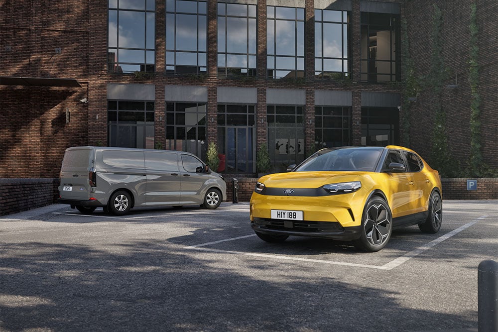  Un fourgon Ford gris et un Capri jaune stationnés devant un bâtiment moderne en briques.