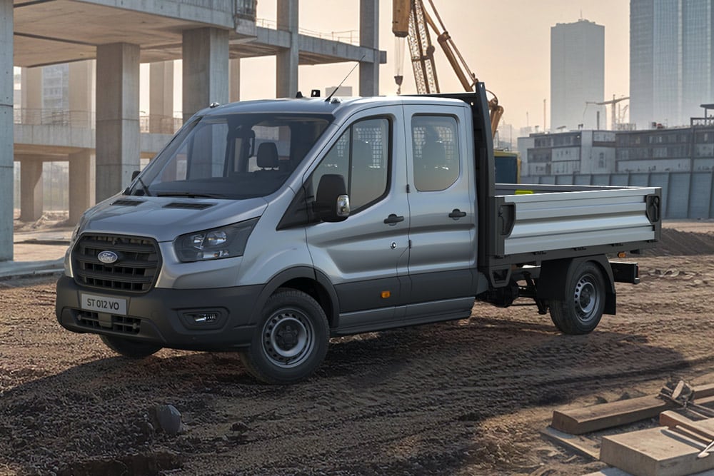 Un camion-benne Ford Transit gris sur un chantier urbain, avec une grue à l'arrière-plan.