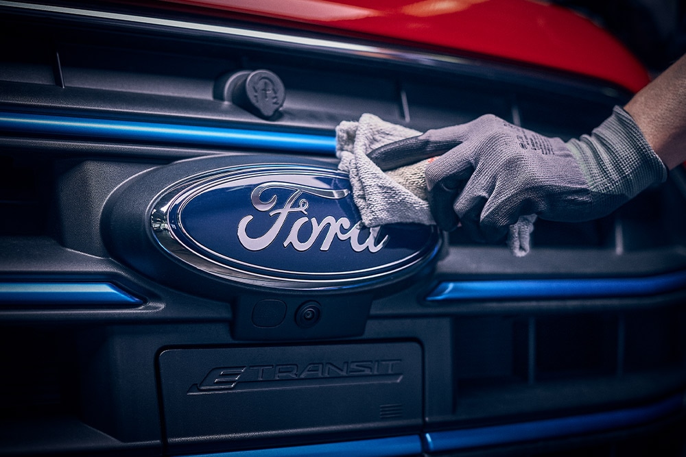 Main gantée touchant l’emblème Ford sur la calandre d’un véhicule.