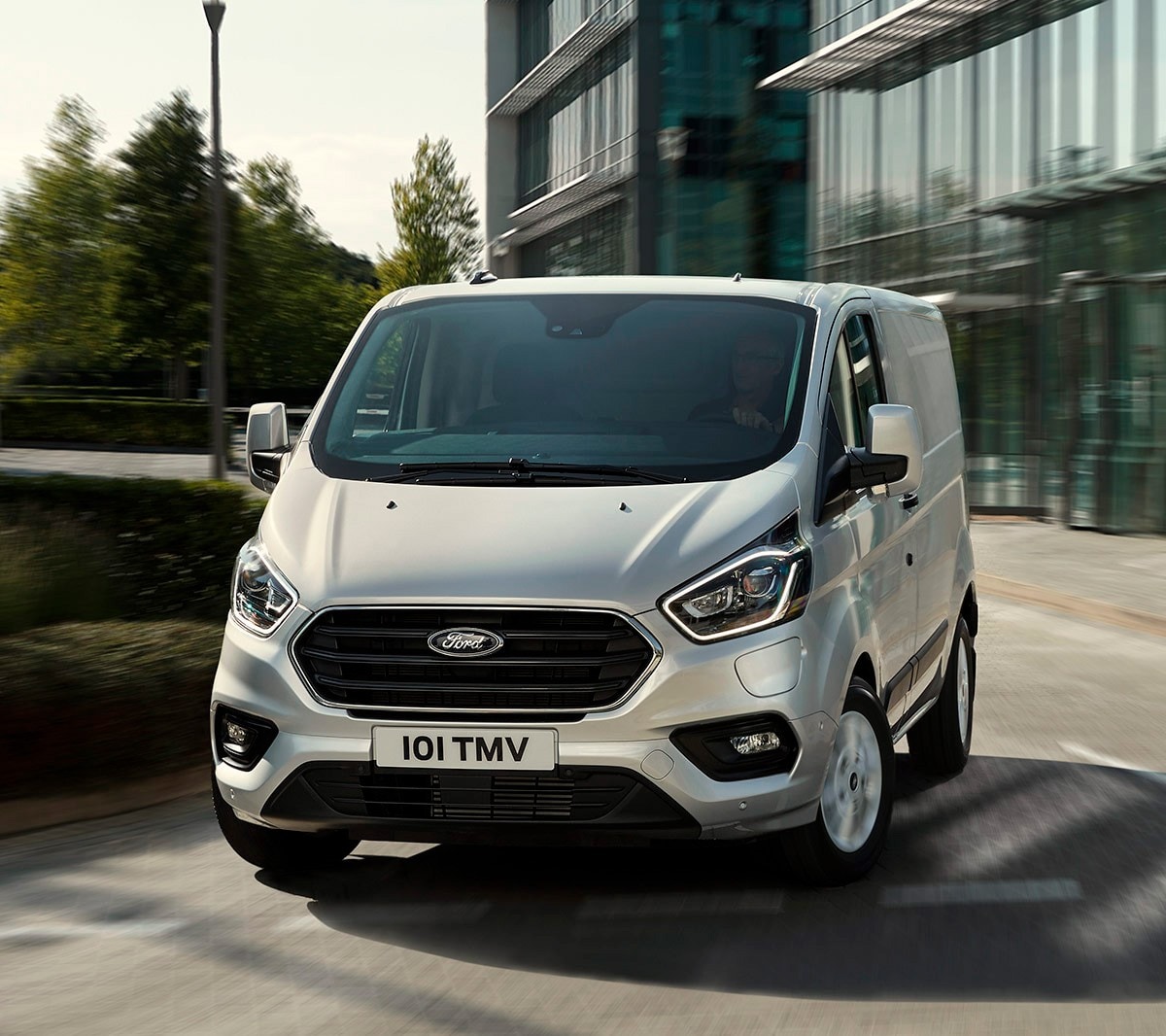 Silver Ford Transit driving in front of glass building