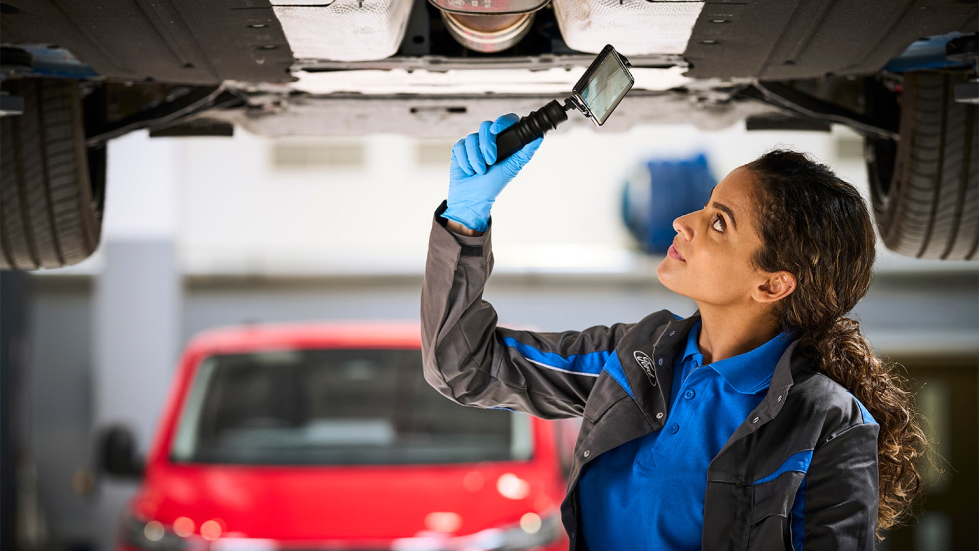 Technicienne utilisant une lampe torche pour inspecter le dessous d’un véhicule sur un pont élévateur.