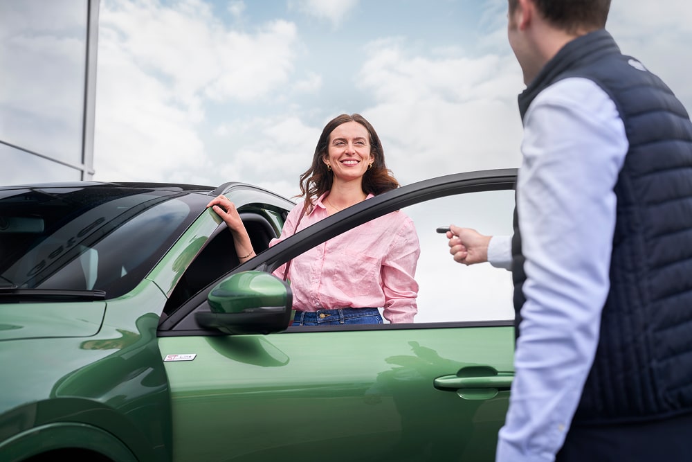Une femme souriant à côté d’une voiture verte, avec un conseiller Ford qui lui remet ses clés de voiture.