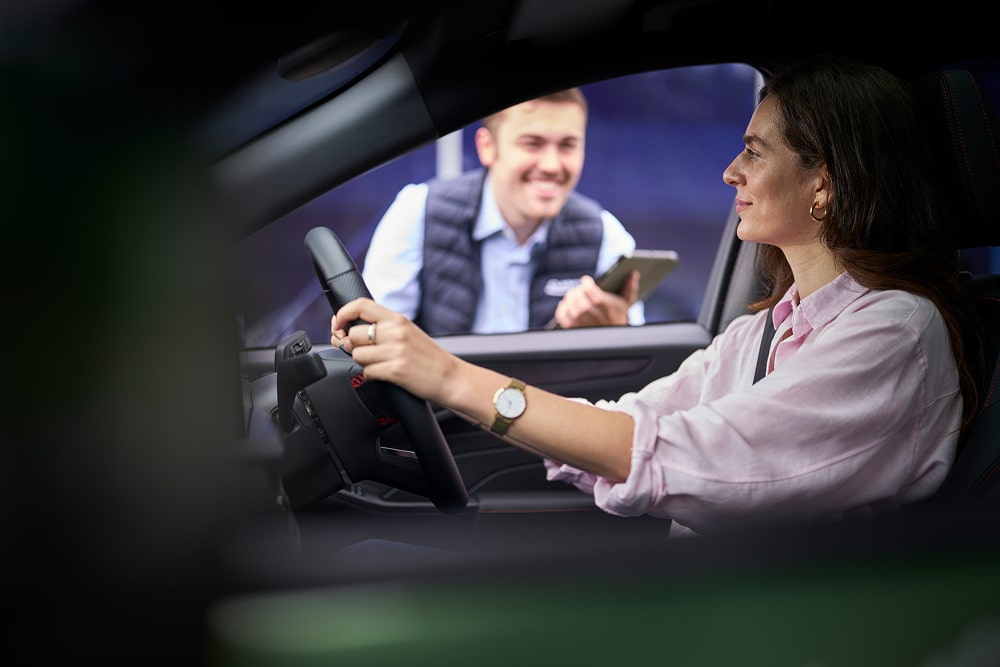 Une femme au volant d’une voiture verte stationnée, en train de sourire à un conseiller Ford visible à travers la vitre.
