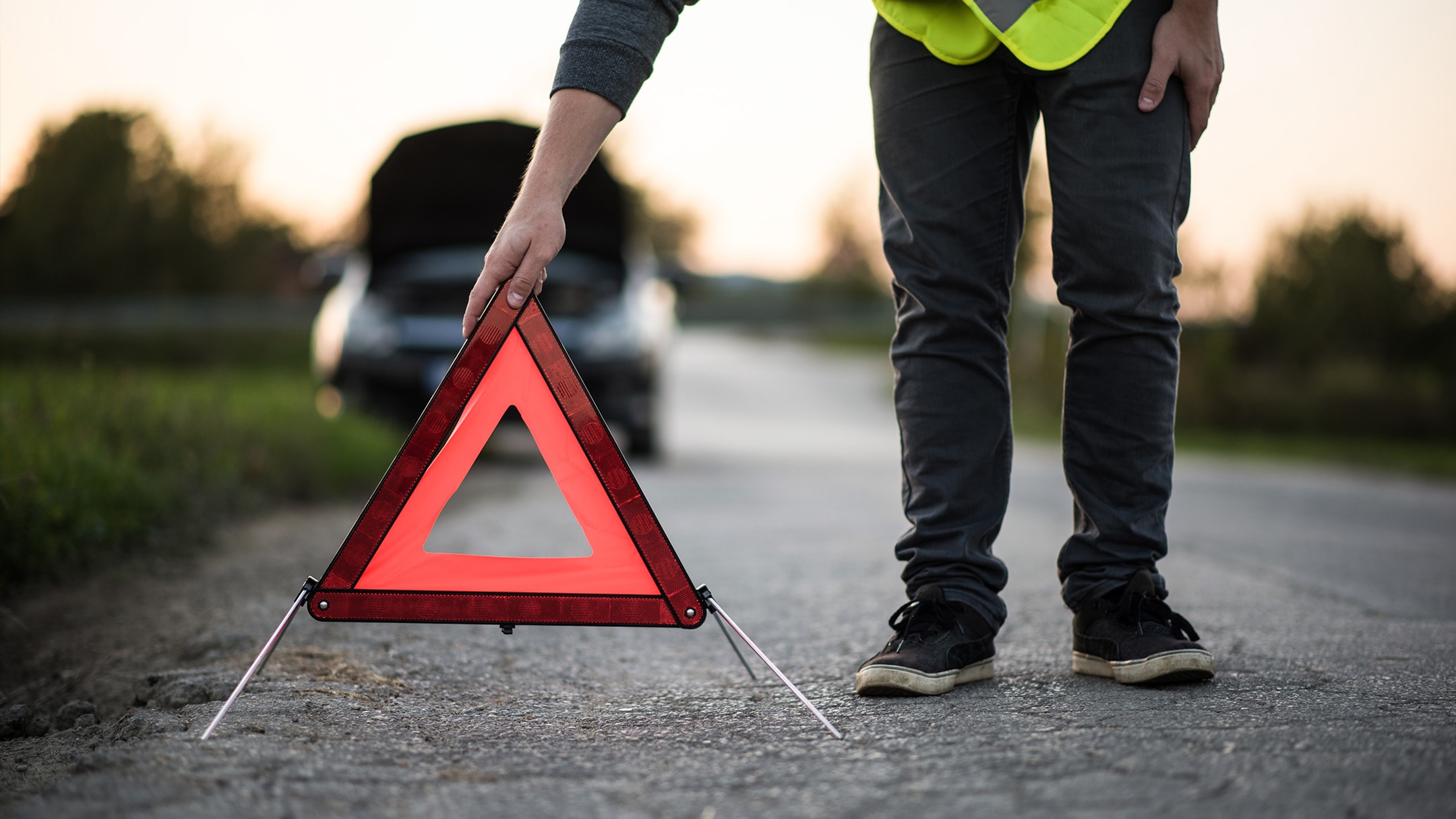 Une personne place un triangle de signalisation près d'une voiture en panne.