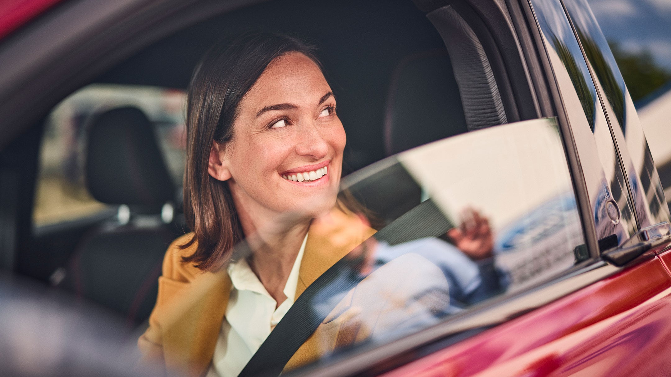 Une personne sourit alors qu'elle est assise dans une voiture Ford rouge.