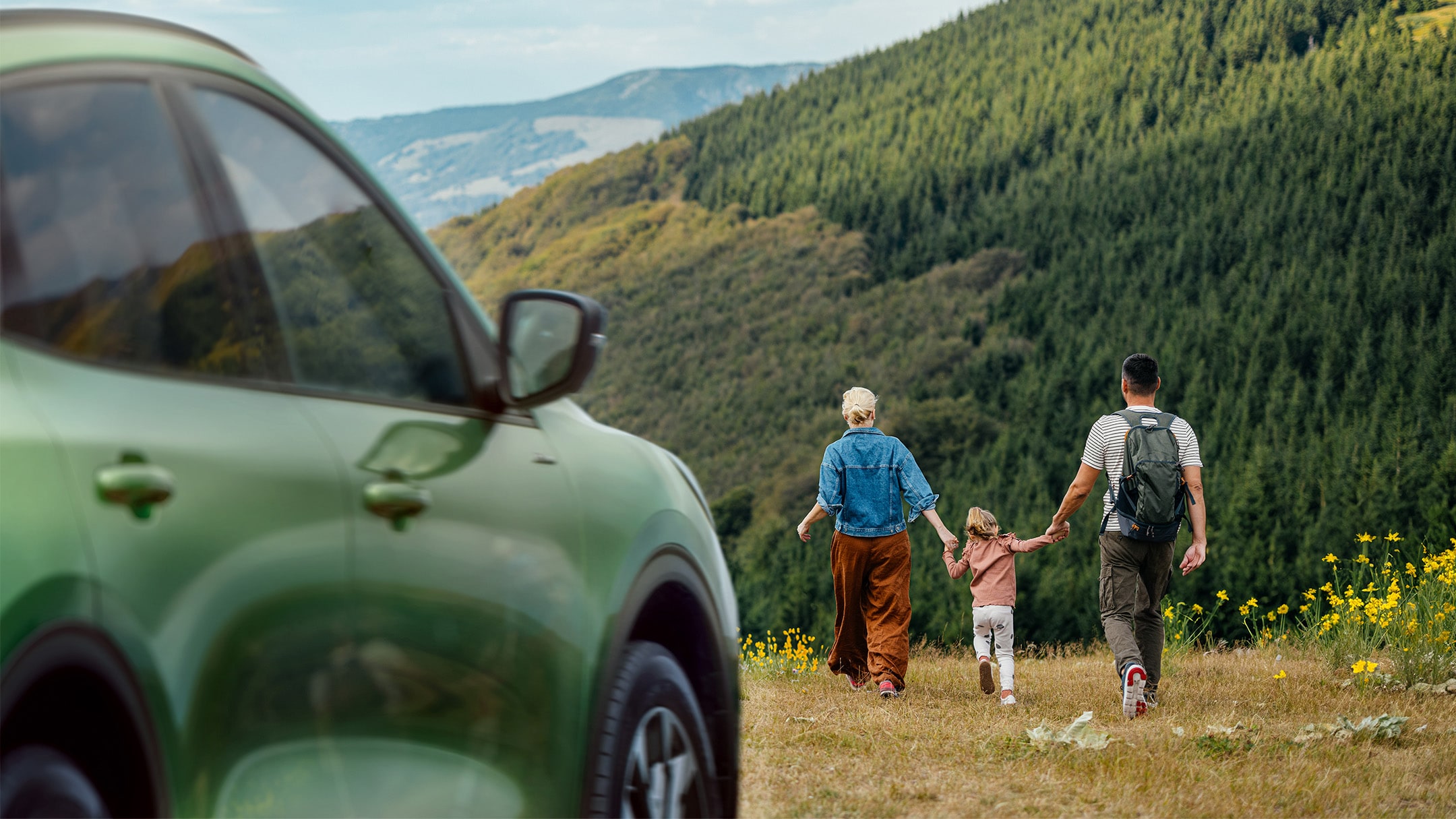 Famille marchant dans un champ à côté d'une Ford Kuga verte
